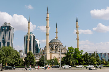 Obraz premium Wide view of the Heart of Chechnya Mosque named after Akhmad Kadyrov, with tall minarets, trees, cars and pedestrians in Grozny, Chechnya, Russia