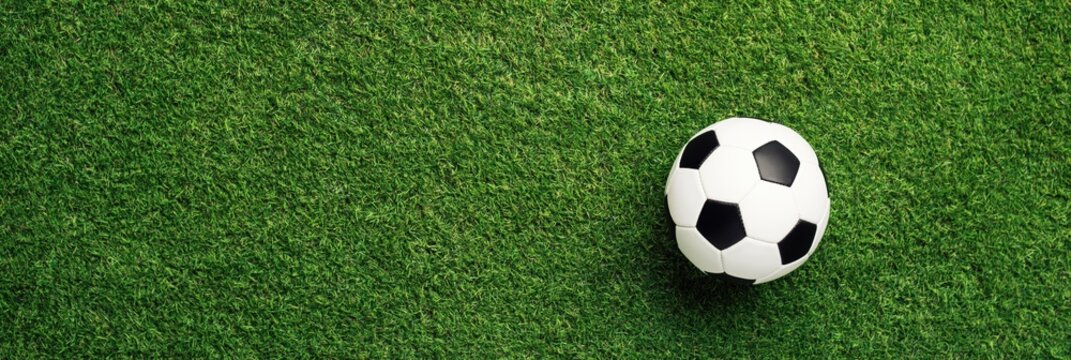 High angle top down view of traditional black and white soccer ball placed on lush green artificial grass field representing sports and training. High quality photo