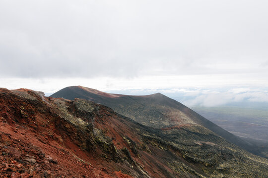 Wide landscape view of rugged volcanic ridge with red scoria and dark lava fields in the North Breakthrough area, Kamchatka Krai, Russia, on an overcast day