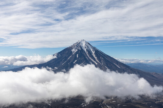 Dramatic view of Koryaksky Sopka stratovolcano summit above a sea of clouds, Kamchatka Krai, Russia, with snow streaks and wide blue sky