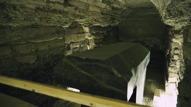 Dark underground corridor with stone arches leading to massive granite sarcophagus inside Serapeum of Saqqara, Egypt, dramatic warm lighting on ancient rock-cut tunnel walls.