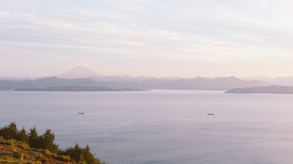 Fototapeta premium Wide panoramic view of Avacha Bay with calm sea, cargo ships and layered mountain silhouettes at dawn, Kamchatka Krai, Russia, serene coastal nature scene