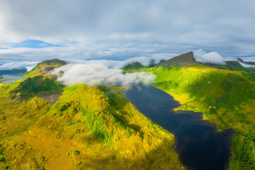 Fototapeta premium Aerial view of misty mountains and fjords in Lofoten, Norway. Atmospheric arctic landscape with fog from a drone. Clouds and scenic northern nature. View from above.