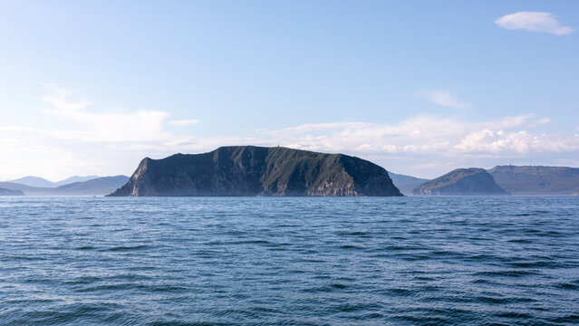 Wide seascape view of a rocky island in Avacha Bay with gentle waves and clear sky, near Petropavlovsk-Kamchatsky, Kamchatka Krai, Russia