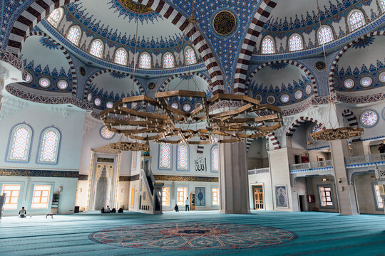 Wide view of the ornate prayer hall inside Borborduk Central Mosque, Kyrgyzstan, featuring patterned dome, chandeliers, stained glass and carpeted floor