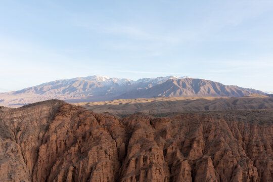 Wide view of Kok-Moinok Canyon with red sandstone cliffs, dry steppe hills and snowcapped mountains under clear sky, scenic nature of Issyk-Kul Region, Kyrgyzstan