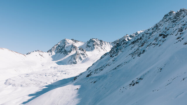 Panoramic winter view of snow-covered mountain ridges and alpine valley near Karakol ski base, Issyk-Kul Region, Kyrgyzstan, with clear sky and bright sunlight