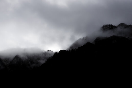 View of dark mountain silhouettes partially hidden by thick white mist and low clouds under a moody sky Hallstatt, Upper Austria, Austria.