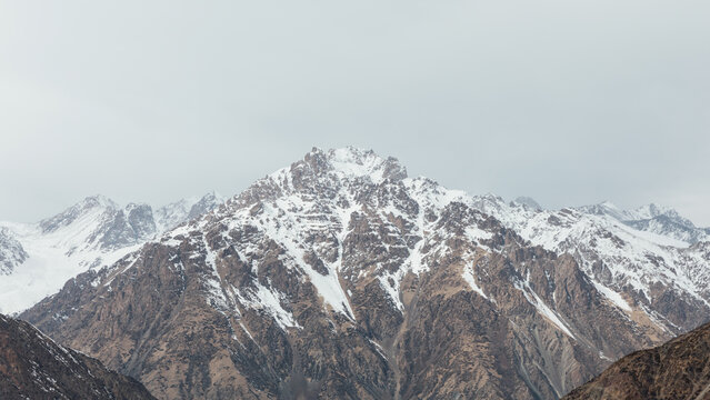 Wide view of snow-covered mountain range and rocky slopes under cloudy sky at Too Ashuu Pass, Chuy Region, Kyrgyzstan, scenic high-altitude landscape