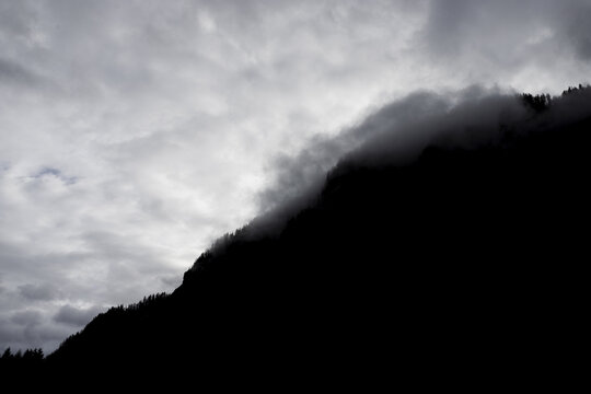 View of the silhouette of a mountain ridge with mist clinging to the slopes under a dramatic overcast sky in Hallstatt, Upper Austria, Austria.