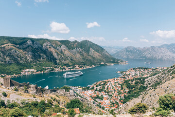 Obraz premium Wide panoramic landscape of Kotor Bay with a cruise ship, mountains and red roof old town seen from the fortress viewpoint in Kotor, Montenegro on a sunny day