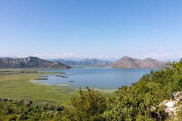 Fototapeta premium Wide panoramic landscape of Lake Skadar with wetlands, calm water and distant mountains on a sunny day, Skadar Lake National Park, Montenegro with copy space