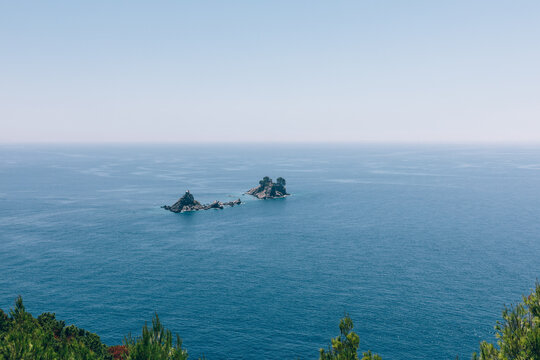 Wide view of calm Adriatic Sea with two small rocky islets on the horizon, photographed from a coastal viewpoint near Petrovac, Budva Municipality, Montenegro