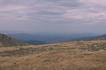 Fototapeta premium Wide panoramic view from Konzhakovsky Kamen of mountain tundra and rocky plateau with layered blue ridgelines and overcast sky, Ural Mountains, Russia