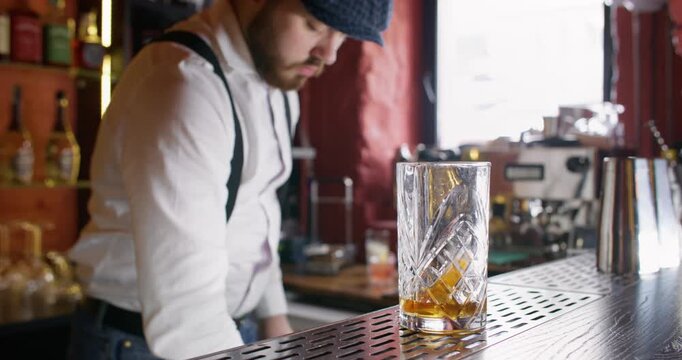Beverage glass. Barista working. Bearded male barman serving cocktail decorating with lemon spiral zest scooping ice cubes mixing drink in cafe.
