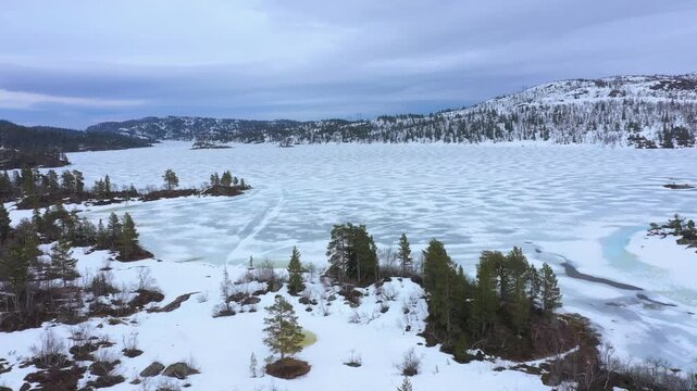 Remote Scandinavian wilderness landscape with frozen lake, melting snow and sparse pine trees near Dalen, Norway, reflecting harsh northern climate and quiet seasonal change