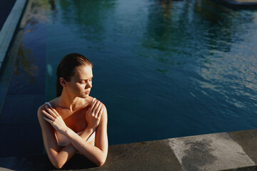 Obraz premium Young woman in swimming pool, relaxing with crossed arms, sunlight on skin, calm water background, peaceful moment, summer lifestyle, natural beauty