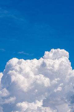 Large sunlit cumulus cloud rising against a clear deep blue sky with calm weather atmosphere.