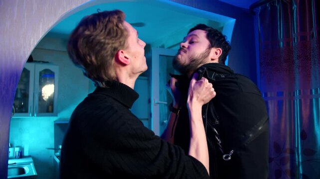 Domestic dispute involving two drunk caucasian males in conflict. Physical confrontation and struggle near doorway at home. A man lifts his opponent by vest. Problem of alcohol and aggressive behavior