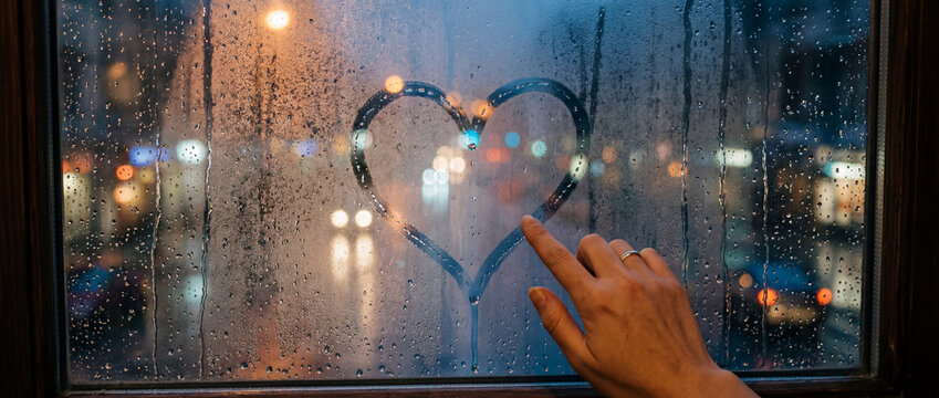 Hand drawing heart shape on rainy window glass