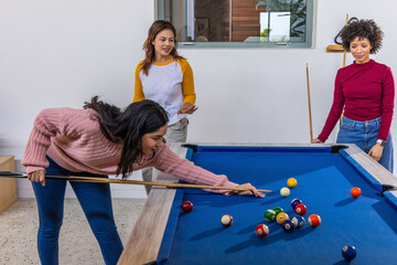 Fototapeta premium Diverse female friends playing billiards in residential game room around blue-felt pool table