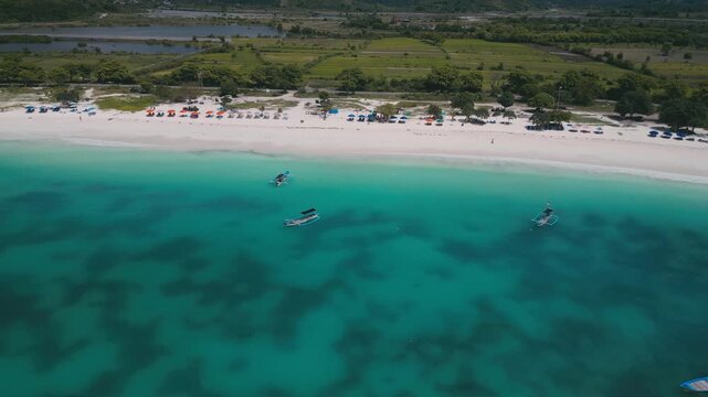 Small Boats Gather By White Sandy Beach. Fishing Boats And Charters Return Over Patterned Seabed. Aerial Perspective Of Vessels And Intricate Seafloor Designs Close To Pristine Beach, Lombok