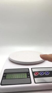 A hand presses the tare button on a digital scale to prepare for measuring green apple 