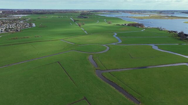 Panoramic aerial view of lush green Dutch polders and meadows crisscrossed by canals. A classic Netherlands landscape featuring a traditional windmill, waterways, and rural countryside scenery.