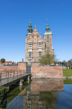 A stunning front view of Rosenborg Castle in Copenhagen, Denmark, with beautiful reflections in the surrounding moat under a clear blue sky.