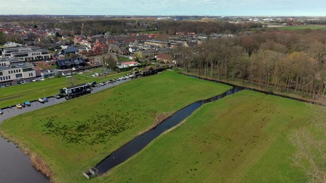 Aerial view of a Dutch suburban neighborhood with houseboats, narrow canals, and green meadows. Scenic landscape of a modern residential area integrated with water and nature in the Netherlands.