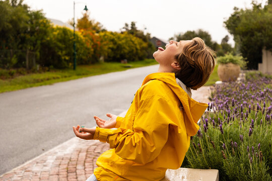 young boy wearing yellow raincoat enjoying the rain