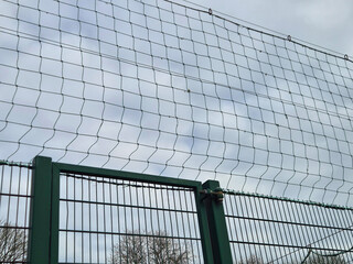Metal fence with protective netting against cloudy sky © Studio-M