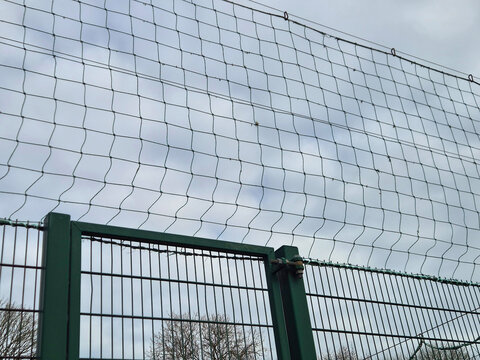 Metal fence with protective netting against cloudy sky