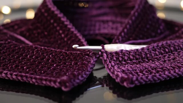 A ball of burgundy yarn and a crochet hook are ready. Handmade crochet work in progress with beautiful dark red yarn.