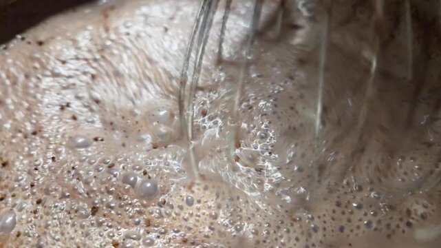 Close-up of bubbling coffee mixture in a pot, showing the swirling motion and frothy texture as it heats up, with steam rising in a kitchen setting