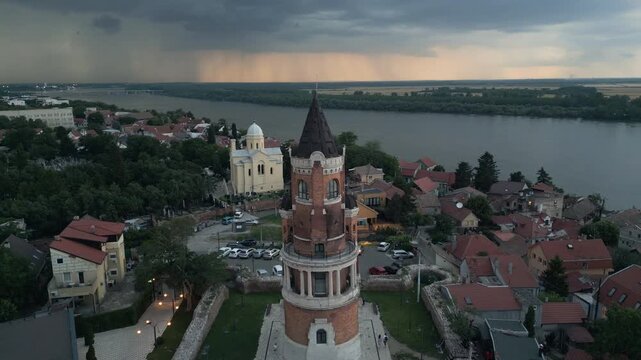 Drone video showcases Gardos Tower in Zemun, wide Danube river and a dramatic twilight sky with active lightning strikes and thunderstorm clouds, Belgrade, Serbia.