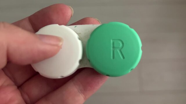 A person holds a contact lens case with white and green sections. The case shows organization for contact lenses at home