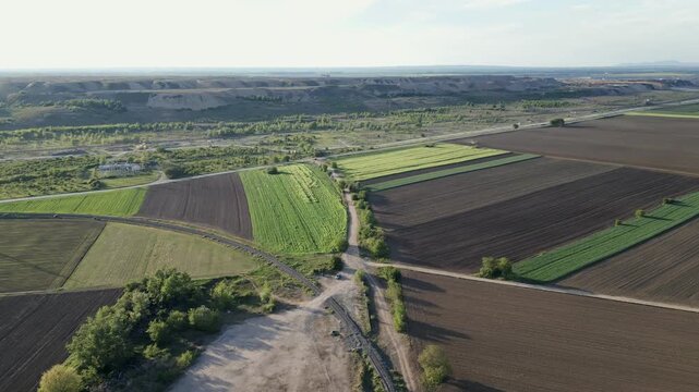 Aerial view of a patchwork of brown plowed soil and green agricultural fields under a clear sunny sky, rural landscape of Eastern Serbia.