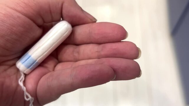 A hand holds a tampon in a bathroom. The moment shows personal care and hygiene. The focus is on the item and its context
