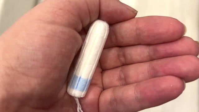 A person is holding a tampon in their hand while in a bathroom. The setting shows a light background and relaxed atmosphere