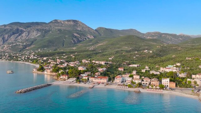 Aerial view of Mikri Mantineia coastal village near Kalamata, Greece, with turquoise sea, beach, breakwater, houses and green mountains in the Peloponnese