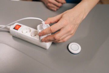 Fototapeta premium Male hands plugging a smart plug into a power strip and pressing its button, illustrating easy setup, remote control, energy saving home automation in a modern indoor setting.