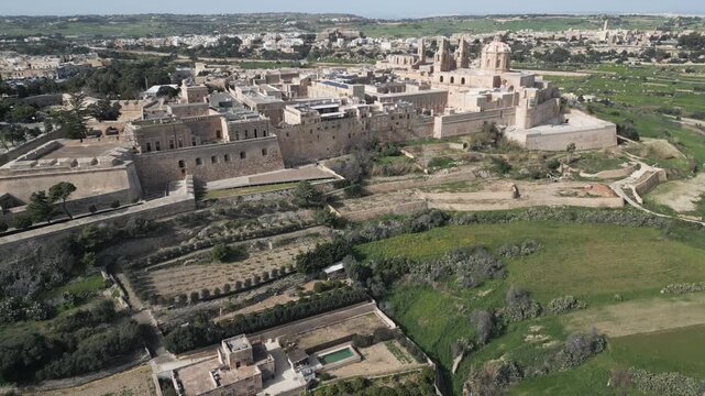 Aerial pull-back shot from Mdina medieval fortifications to rural Malta landscape