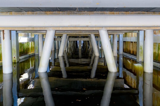 Looking at the metal and concrete supports under a large wharf. Wooden walls on each side enclose the wharf.