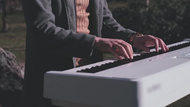 Cinematic close up of pianist hands performing on white digital piano outdoors during golden hour. Artistic music performance with soft natural light, elegant atmosphere