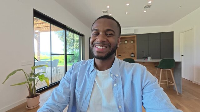 Personal perspective view of a smiling young african american man talking and gesturing during a video conference, working remotely from his modern home office with a view of the outdoors