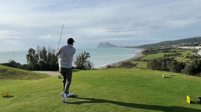 Golfer prepares to swing on a scenic golf course overlooking the ocean with mountains and coastline in the background