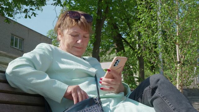 Elderly lady with poor eyesight changes sunglasses to reading glasses for vision correction to use phone on park bench. Concept of presbyopia, age related farsightedness and senior health.
