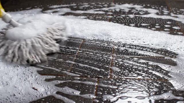 Closeup of a person mopping a dark tiled floor with soapy water