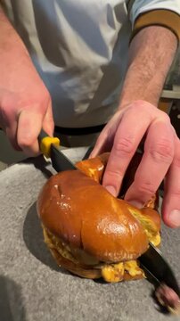 Chef slicing a delicious burger with a sharp knife on a round gray plate in a modern kitchen setting